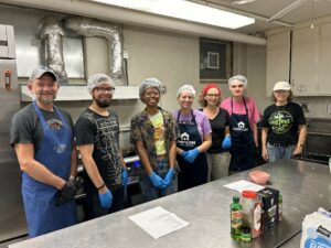 Seven volunteers stand in hairnets and smile at the camera.